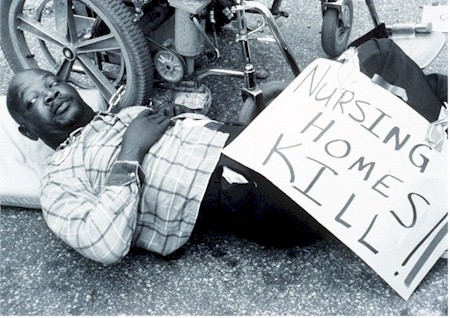 In this black and white photograph, 
      a man is lying on his back beside his wheel chair. Description follows.